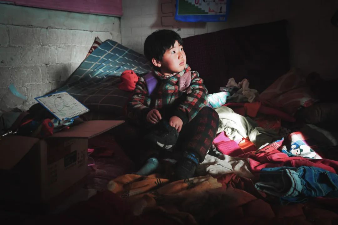 楠楠背着书包蹲坐在炕上看着窗外。