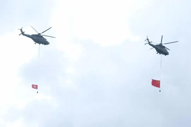 飞行服务队两架分别悬挂国旗及区旗的直升机，飞过维港上空 图源：香港文汇报