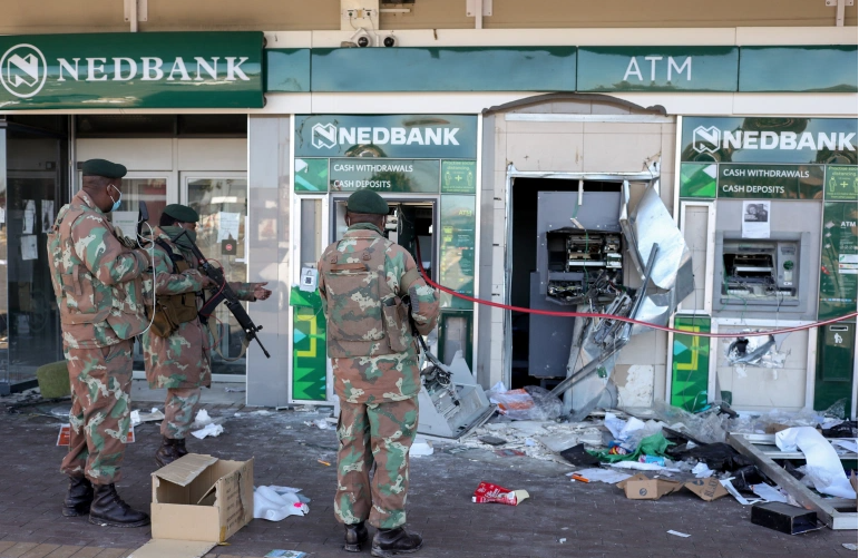 ▲当地时间7月13日，南非国防军士兵查看银行外被砸毁的ATM机。图据路透社