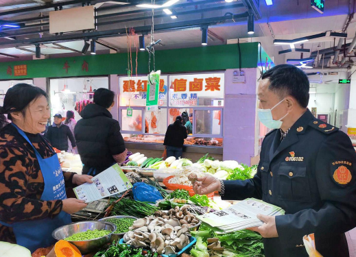 图为监管人员在农贸市场蔬菜摊位开展宣传.