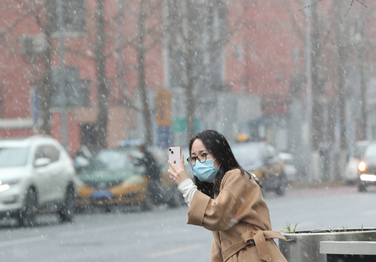 3月17日，北京市东城区东直门，一名女士拍摄雪景。中国日报记者 邹红 摄