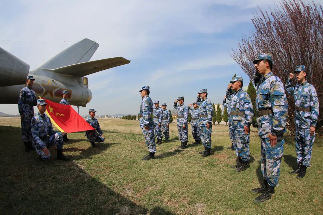 ▲海军航空兵某场站官兵们面向军旗举起右拳，用铮铮誓言为海军庆生。