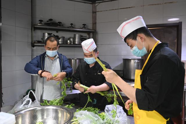5月19日,朱希明(左)在自家餐厅的厨房里与厨师一起择菜洗菜.