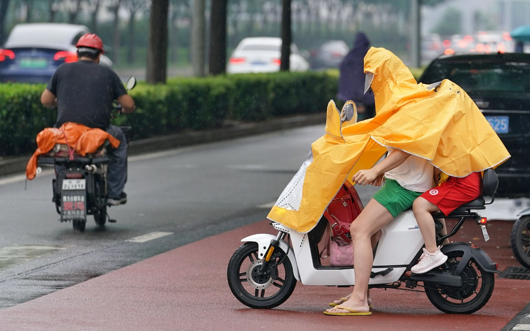 6月27日,广渠路上,一位家长骑电动车送孩子上学,小朋友给家长举着雨伞