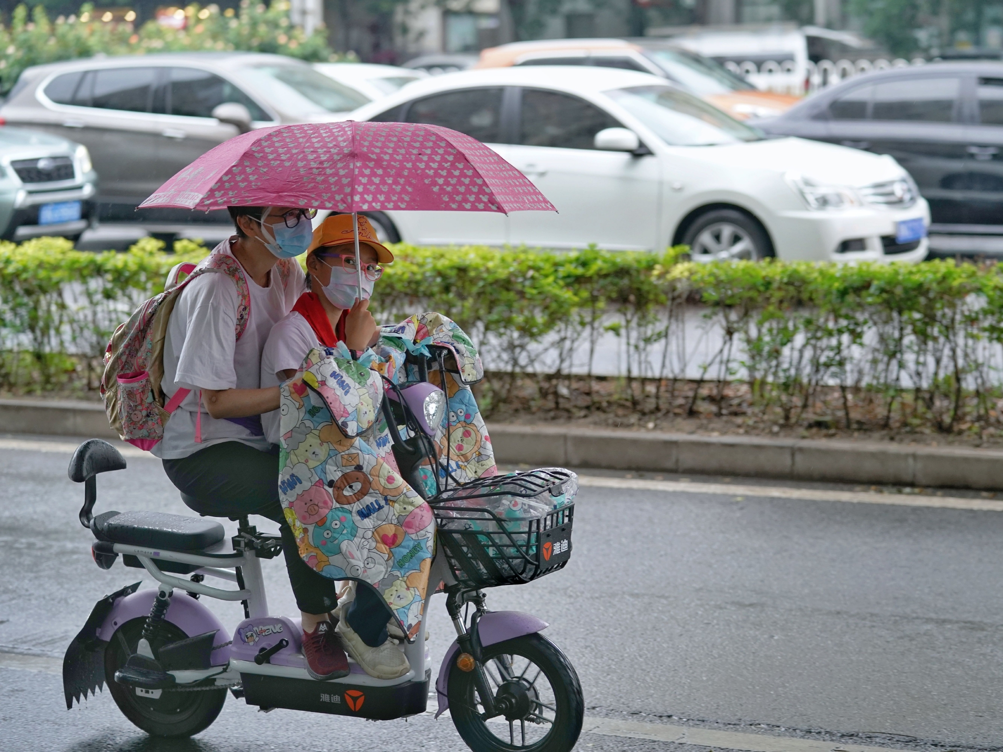 6月27日,广渠路上,一位家长骑电动车送孩子上学,小朋友给家长举着雨伞