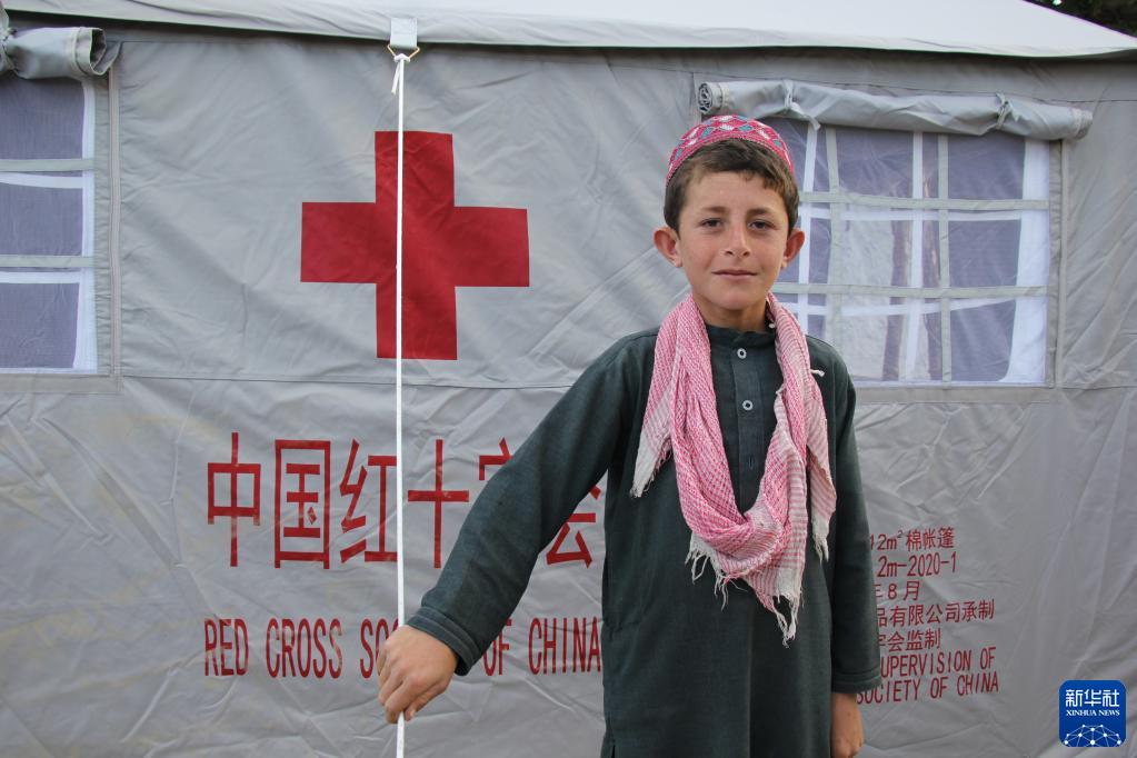 7月18日，在阿富汗地震重灾区帕克提卡省齐鲁克区，一名男孩站在中国红十字会援助的救灾帐篷外。新华社发（萨巴文摄）