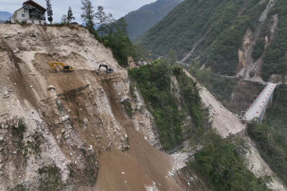 9月6日，泸定县磨西镇通往海螺沟景区的道路被山体滑坡阻断，蜀道集团工作人员通过挖机在绝壁之上全力抢通道路。（杨树 摄）