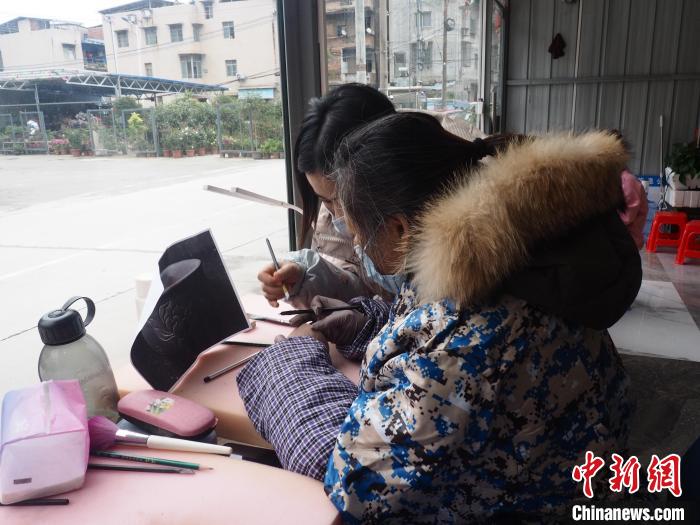 图为一位残疾人(右)在杯子上雕刻荷花，其成品多通过线上渠道售出。李娇阳 摄