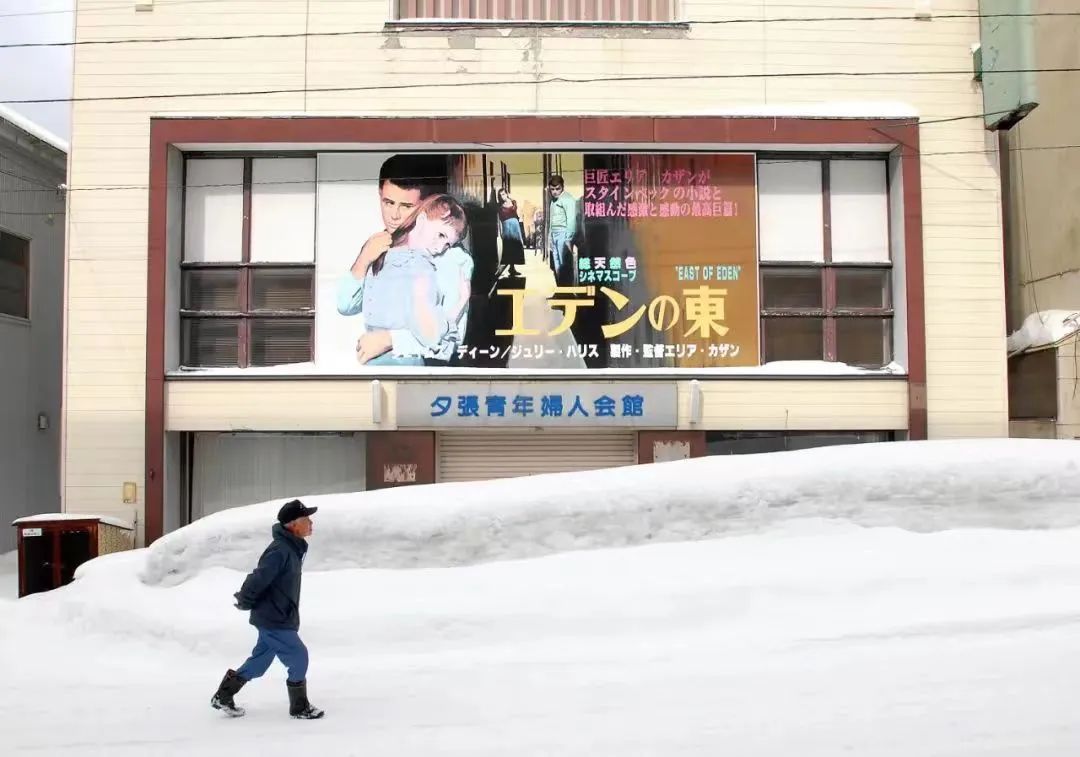 2007年3月13日，日本夕张，一位居民雪天走过一栋挂着电影海报的废弃会馆。夕张年均气温低于6℃，一年有一半时间被雪覆盖（视觉中国 供图）