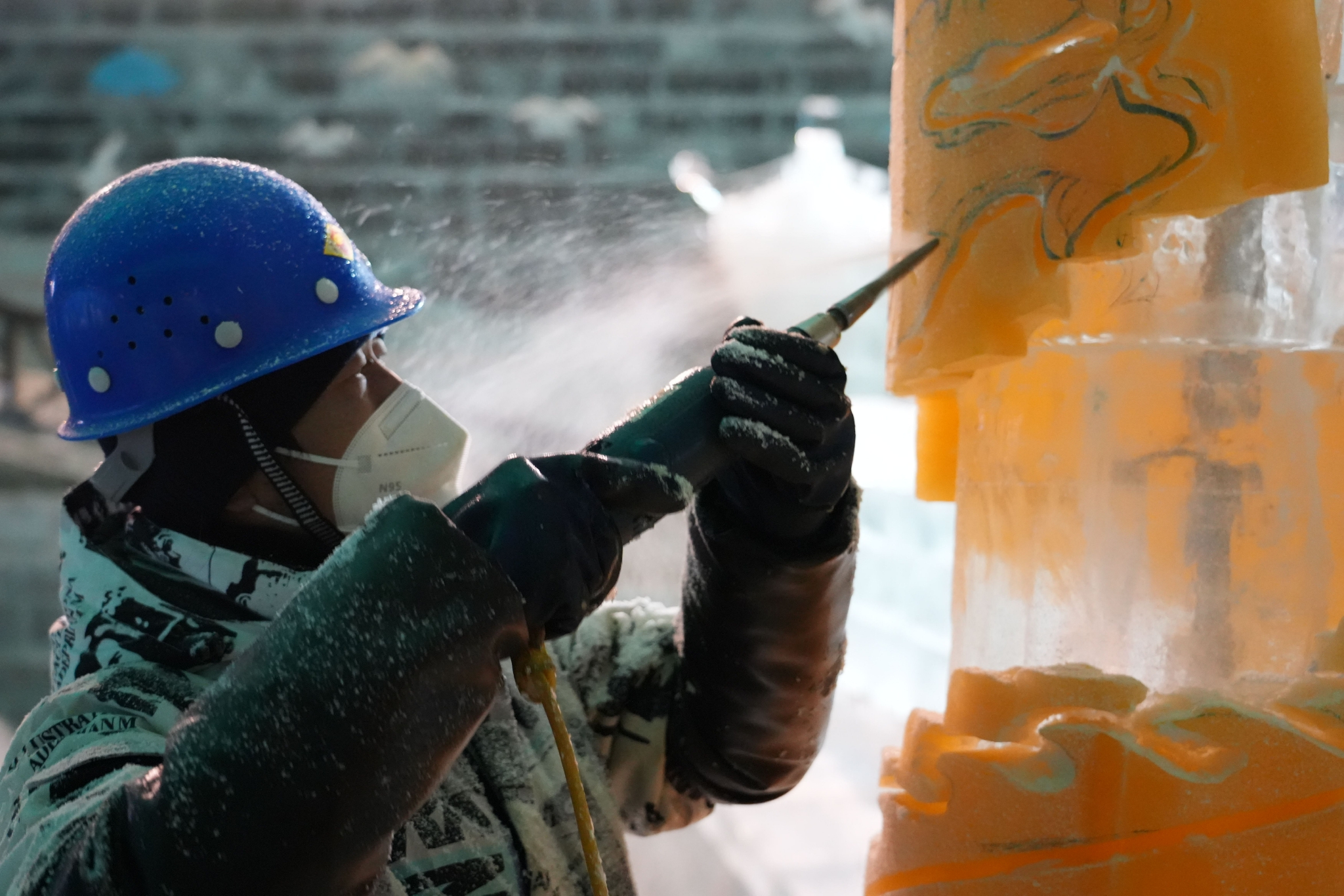 冰雕师傅手中的电钻快速旋转,冰花飞溅到冰雕师傅的衣服和安全帽上.