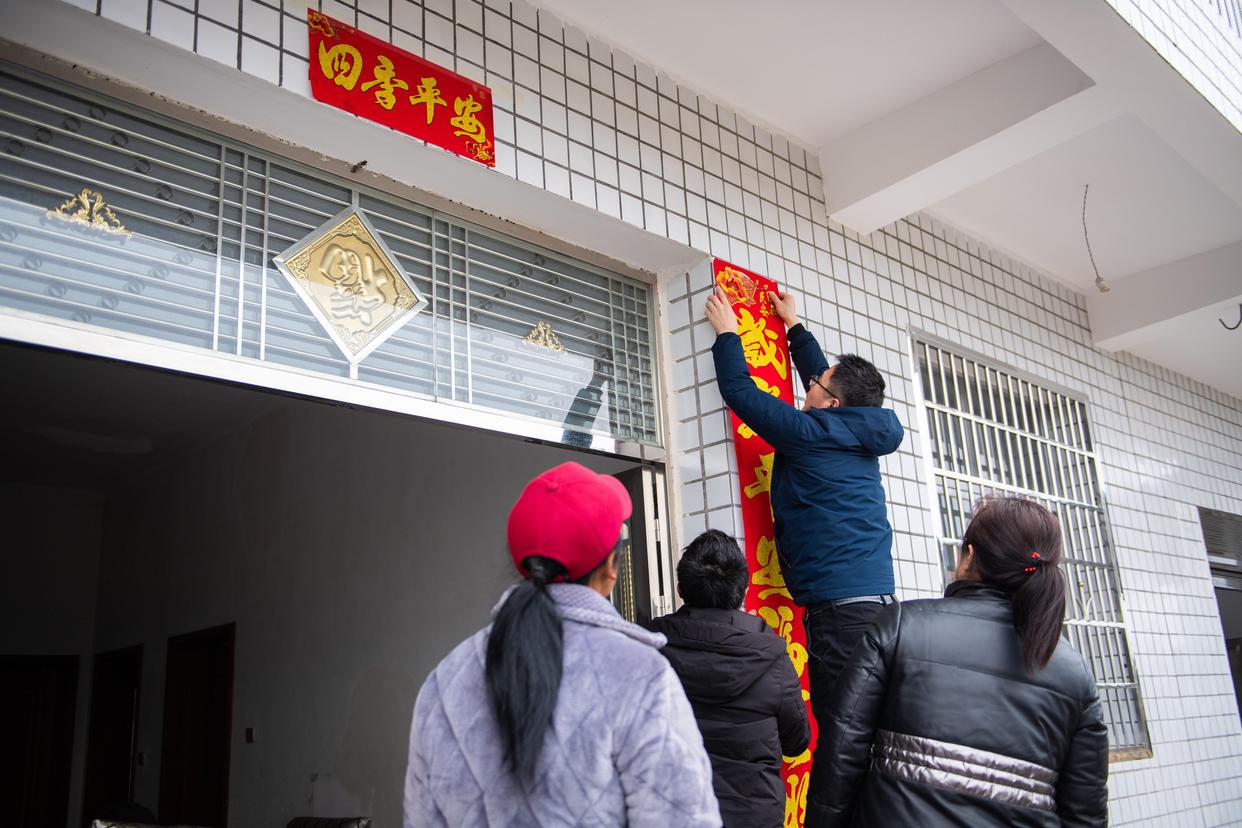 街道老鹳树社区,乡村振兴驻村工作队队员程鹏(右二)给脱贫户家贴春联