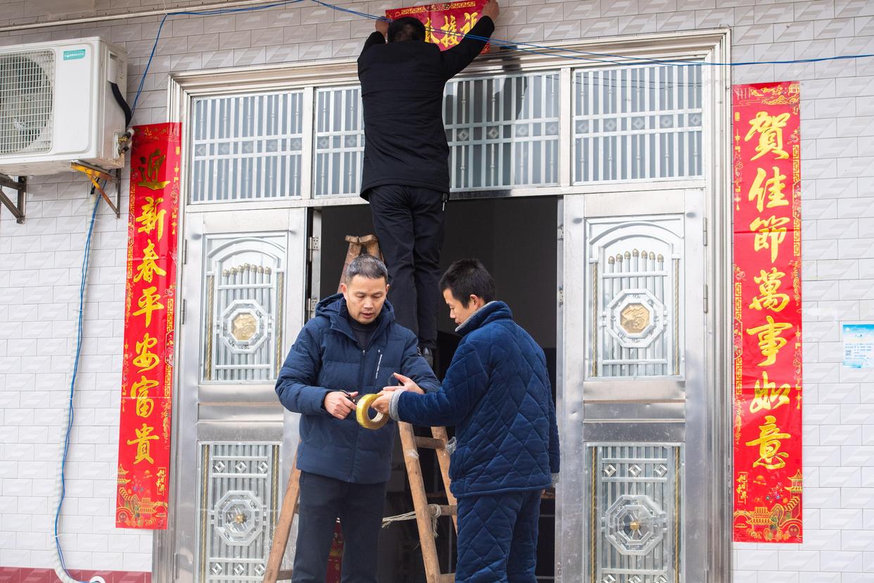 乡村振兴驻村工作队成员和脱贫户(右一)一起贴春联