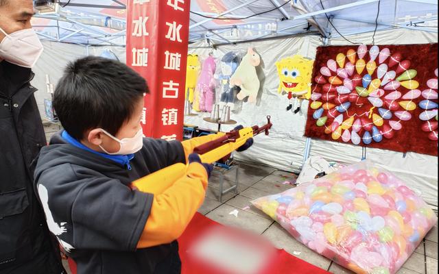 打气球的小摊前,小朋友在家长的陪同下尝试瞄准靶心的红色气球.