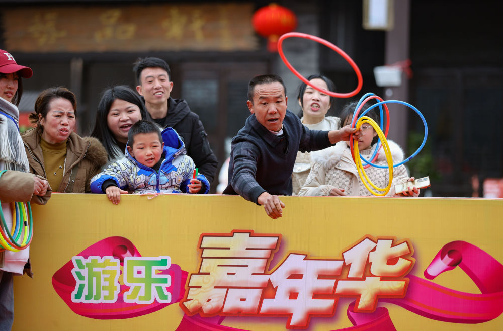 游客在贵州省黔东南苗族侗族自治州丹寨县万达小镇庙会上玩套圈游戏