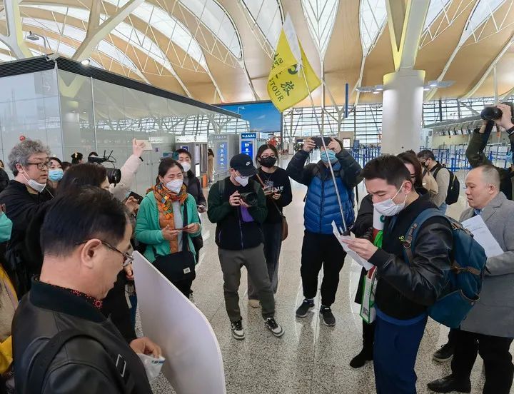 2月6日，在上海浦东国际机场，出境团队游领队师文（举旗者）向游客说明相关注意事项。图片来源：新华社