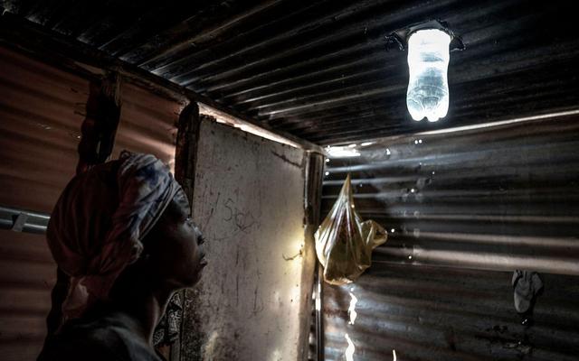 当地时间2023年2月6日，南非豪登省，一名居民在她的棚屋里看着使用矿泉水瓶自制的照明装置。图/视觉中国