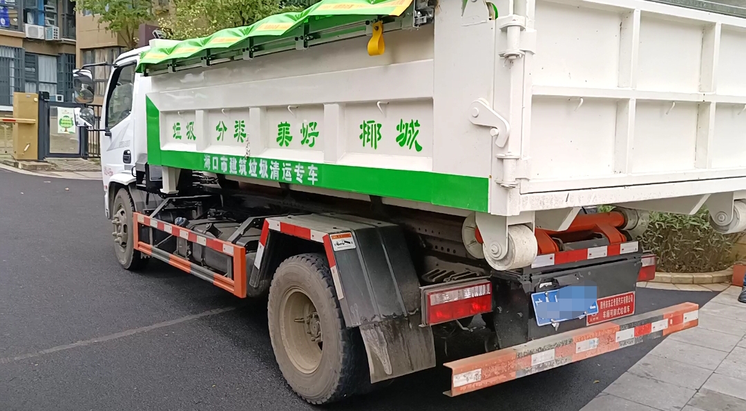 图为清运车辆将移动式建筑垃圾箱运到小区