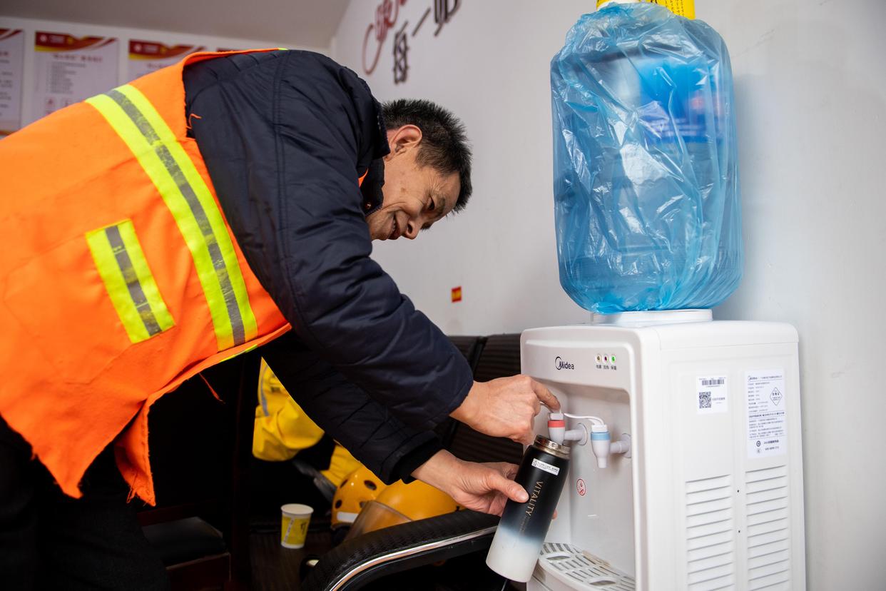 2月16日,在汨罗市归义镇友谊河社区"暖心驿站",一名环卫工在接热水.