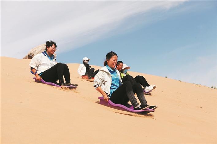在六师红旗农场北庭沙漠生态旅游景区,游客体验滑沙乐趣(资料图片).