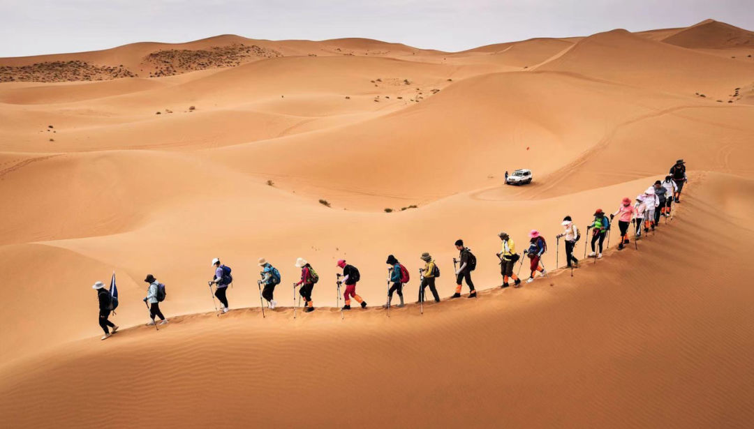 在沙漠里徒步，需要跟从领队沿着沙脊行进（图为2021年7月11日拍摄的内蒙古阿拉善腾格里沙漠中的徒步队伍）（张铮 摄 / 视觉中国 供图）