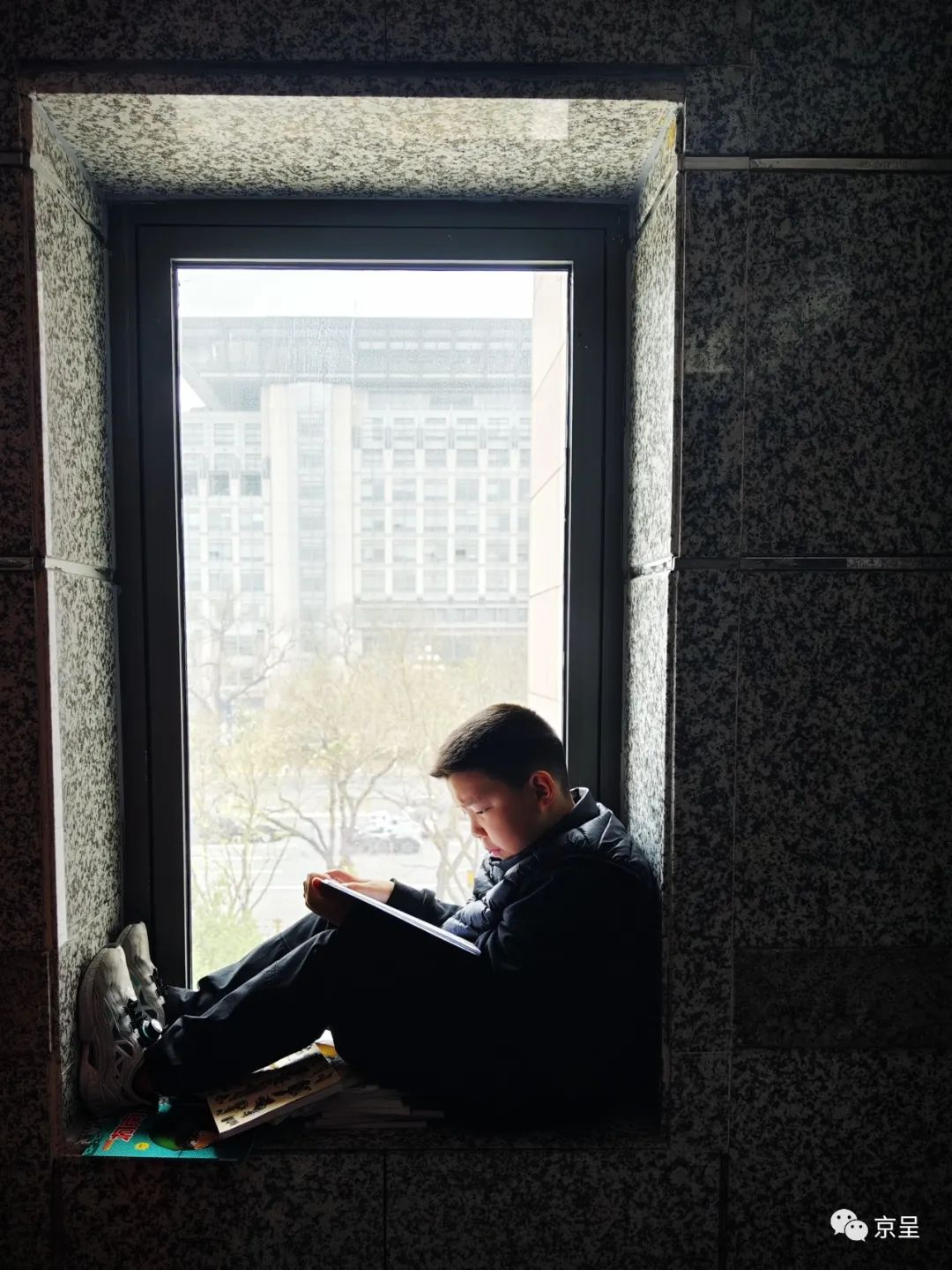 北京西单图书大厦,一位男孩坐在窗前"借光"认真看书.