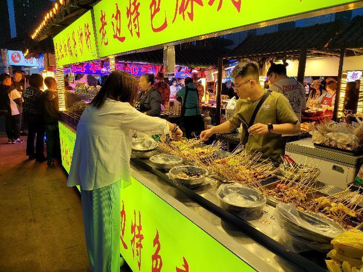 图为沈阳塔湾兴顺夜市,一位旅客正在购买美食.