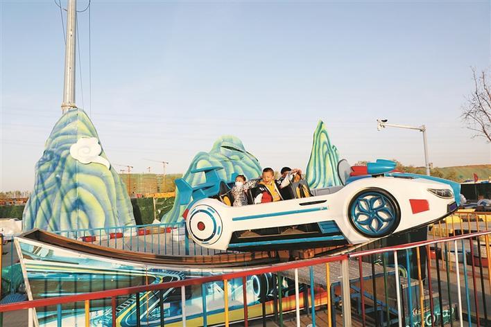 在十二师亚心花海主题乐园,孩子们体验旋转飞车娱乐项目(摄于5月15日)