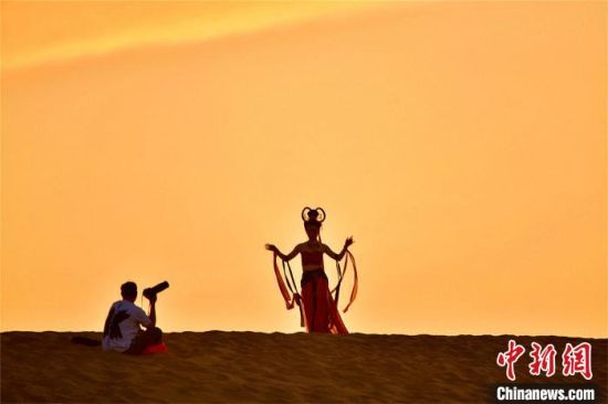 2023年6月7日,游客身着特色服饰和自己的旅拍团队在鸣沙山上拍摄敦 