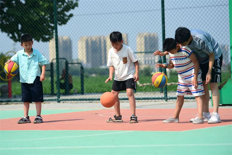 7月10日,在河北沧州,志愿者周义帛(右一)教建设大街社区的孩子打篮球.