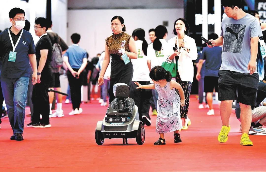 小观众在展览现场偶遇场地内的机器人，两者热情互动。北京日报记者 和冠欣摄