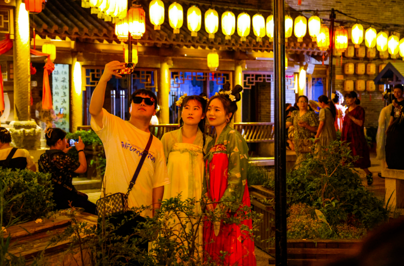 夜色下的洛阳洛邑古城灯火璀璨,身着汉服的游客在古城内自拍.