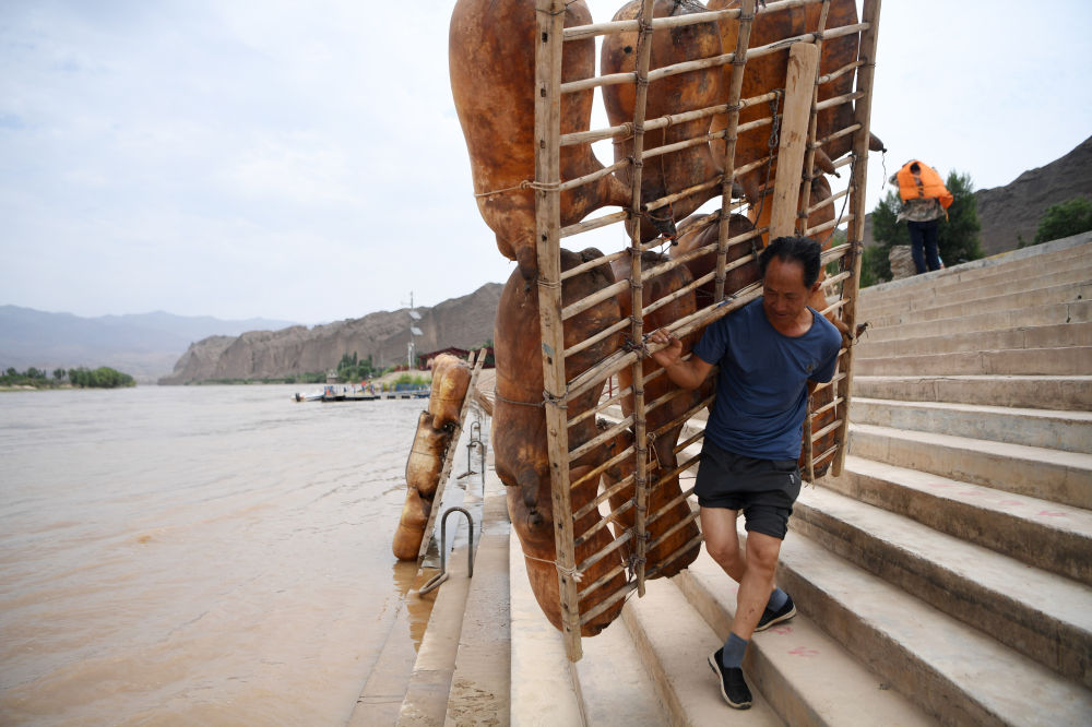 一名筏子客在黄河石林景区背着羊皮筏子准备漂流(7月11日摄).