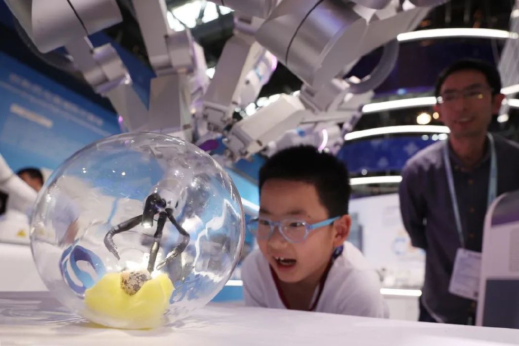 小朋友在2023中关村论坛展览（科博会）上观看单孔腔镜手术机器人剥一枚生鹌鹑蛋。