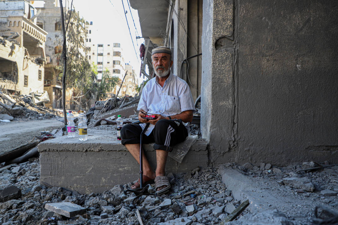 ↑10月12日，在加沙城，一名男子坐在被以色列空袭炸毁的建筑旁 图据新华社