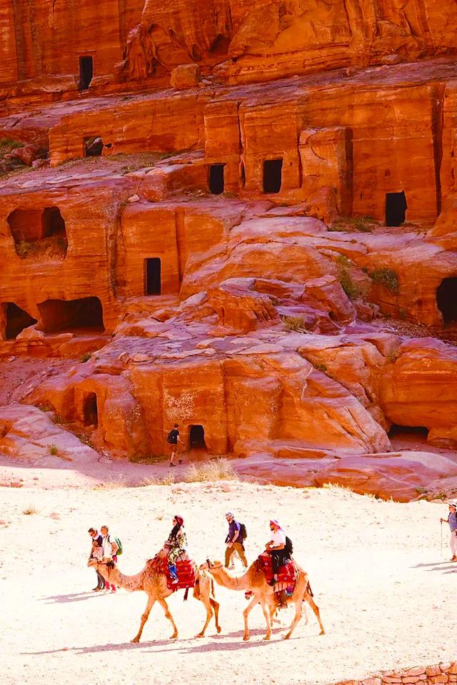 图片说明： 几名骑骆驼的西方游客正从纳伯特人居住的岩洞前走过。