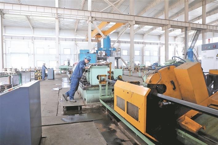 在新疆金鑫利达钢管有限公司生产车间内,工人在操作机械切割钢板(资料