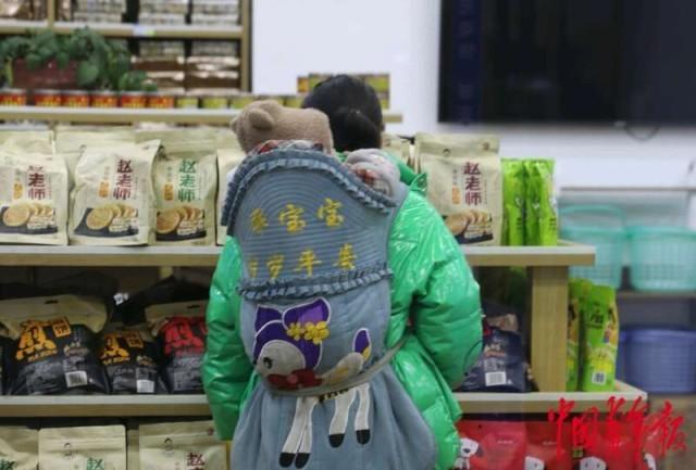 2月12日，重庆北站候车大厅一处便利店，一名背着孩子的母亲在选购食品。中青报·中青网记者 陈剑／摄