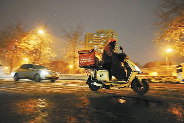 外卖员谨慎骑行，在城市中冒雪穿梭。本报记者 程功摄