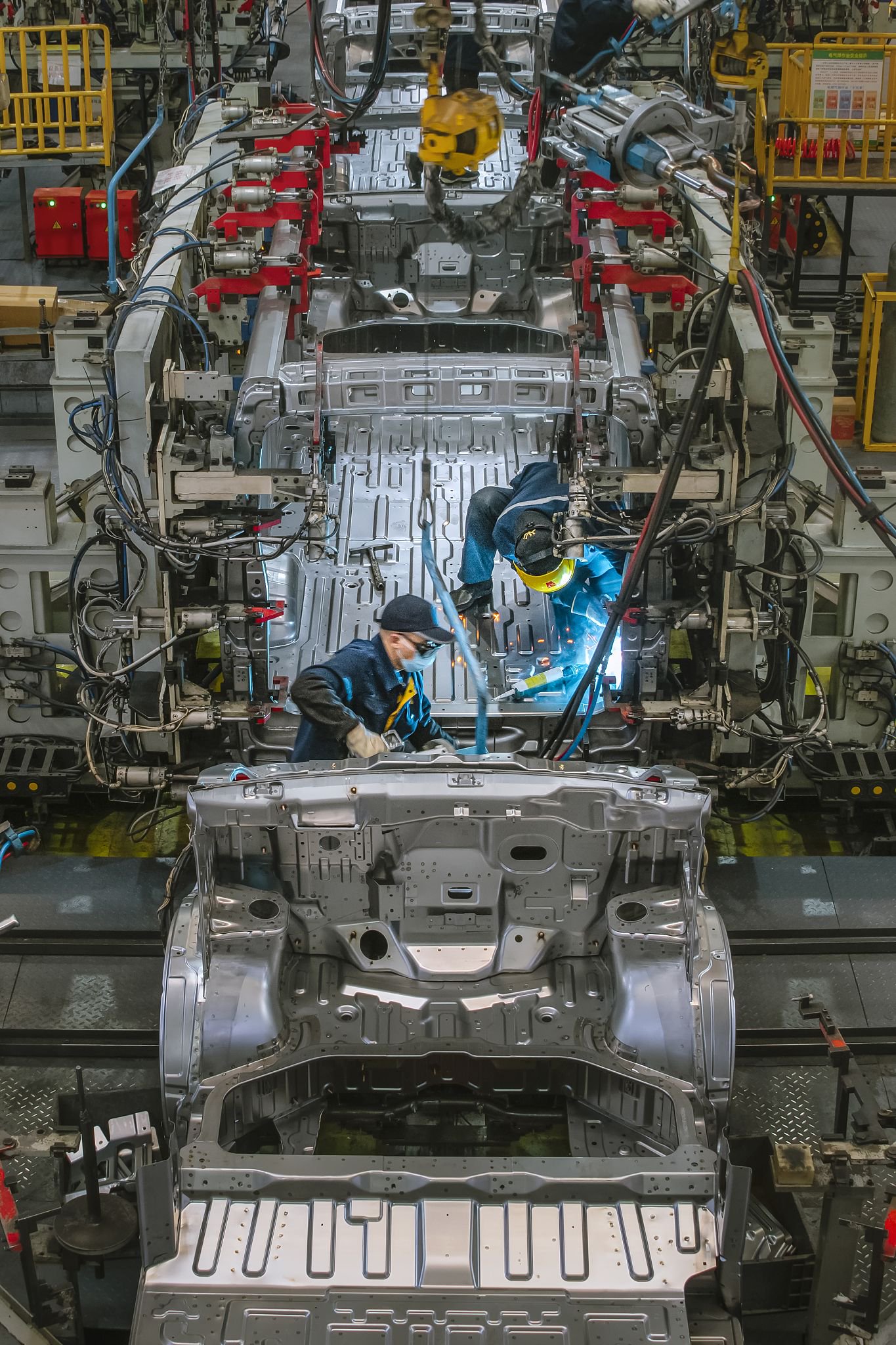 一家商用新能源汽车生产企业的冲焊车间,工人们正在生产线上焊接车身