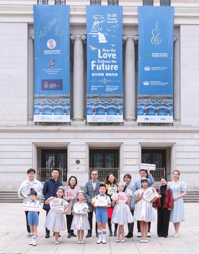 参加“听见所爱·拥抱未来”慈善音乐会的嘉宾和天津小海豚听障儿童合唱团的成员在上海音乐厅巨幅海报前合影留念。