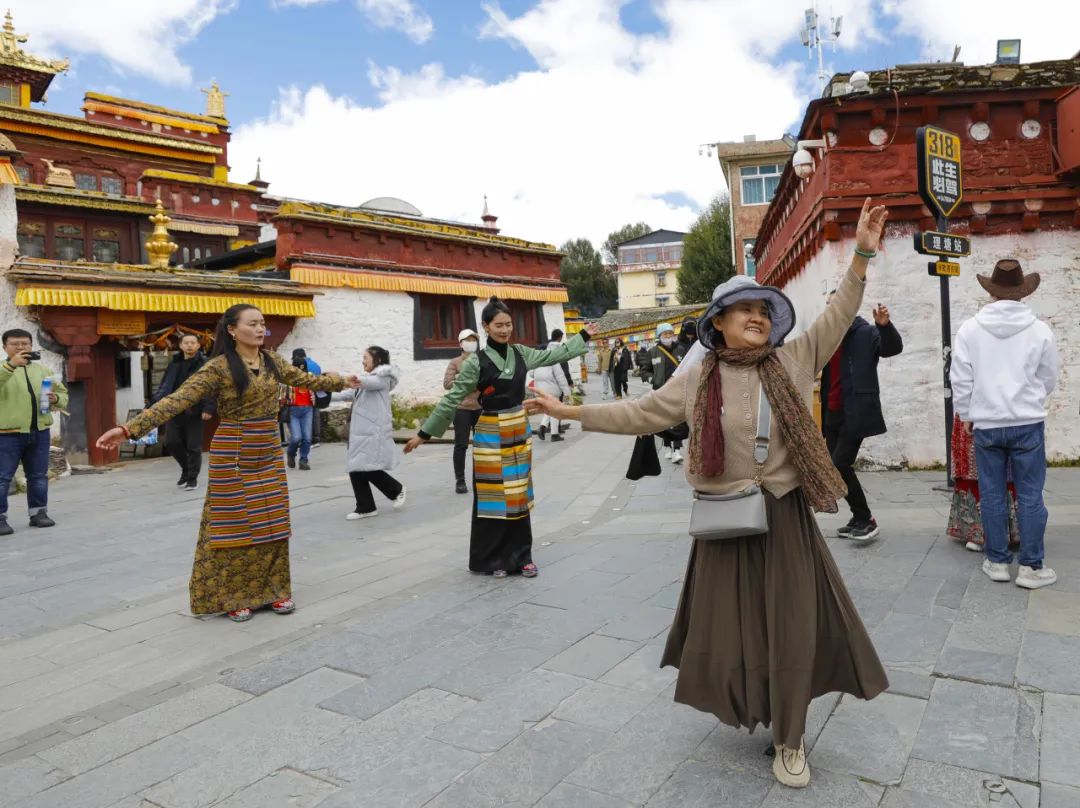 ▲2023年10月10日，游客（前）在理塘县勒通古镇跟着当地藏族群众跳锅庄舞。新华社记者 沈伯韩 摄