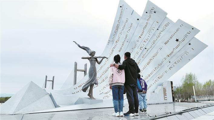 孙海波在四师可克达拉市《草原之夜》雕塑前为女儿讲述父辈屯垦戍边的故事（摄于4月10日）。李惠 崔凯 摄