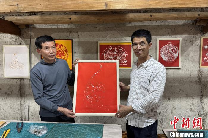林长聪(右)展示刻纸作品《猛虎下山》。柯宁 摄