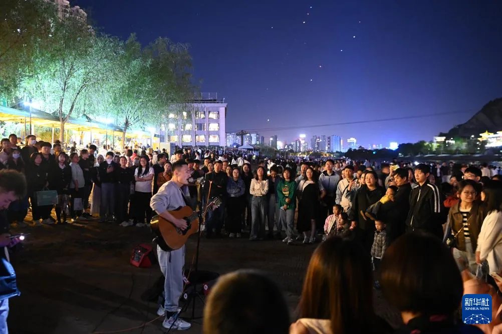 4月23日，在兰州市城关区的黄河兰州段近水平台，市民及游客观看音乐爱好者弹唱。新华社记者 范培珅/摄