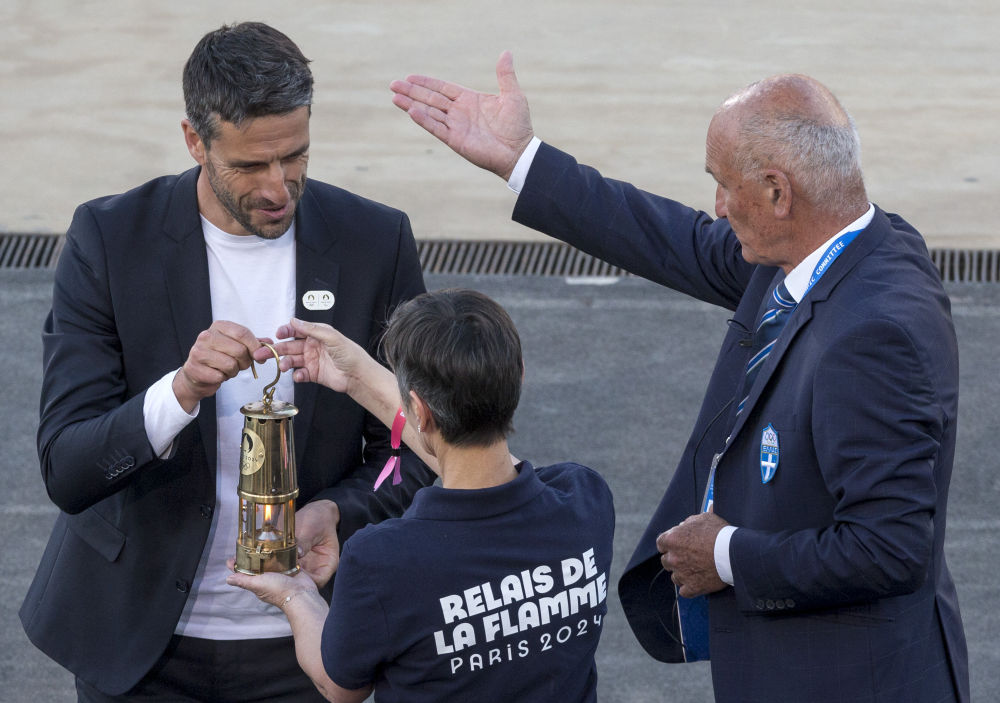 4月26日，巴黎奥组委主席埃斯坦盖（左）将巴黎奥运会火种灯交给工作人员。新华社发（马里奥斯·罗洛斯摄）