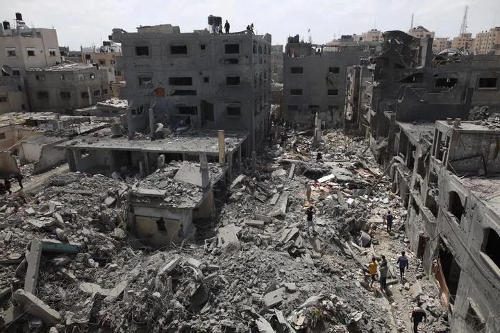 4月27日，在加沙地带中部努赛赖特难民营，巴勒斯坦人走过以军空袭后的废墟。新华社发