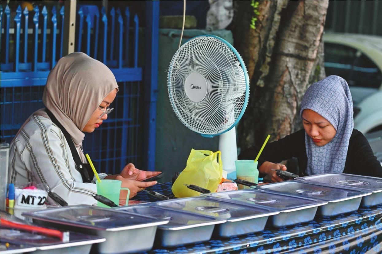 下图：4月25日，在马来西亚吉隆坡，食品摊位的商贩用风扇降温。