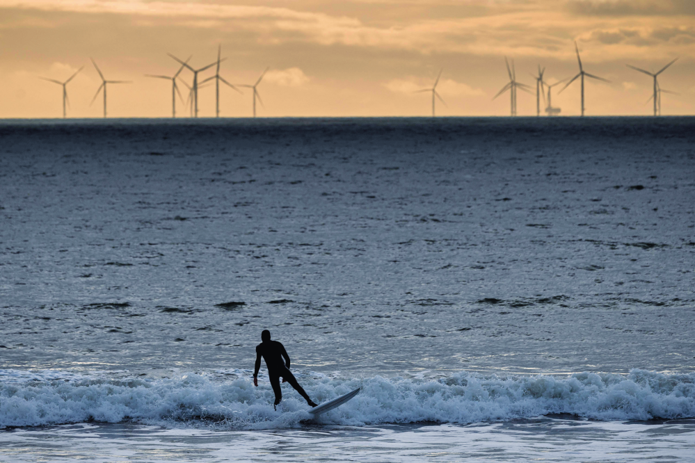 在法国拉博勒，一名男子在海上风力发电场附近的海域冲浪（2023 年 1 月 5 日摄） 新华社 / 法新
