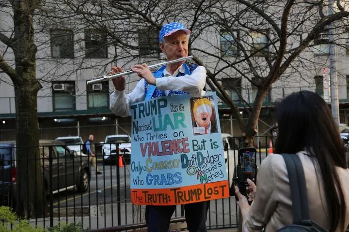 4月15日，在美国纽约，美国前总统特朗普的反对者在法庭前的公园挂着标语牌演奏乐器。新华社记者刘亚南摄
