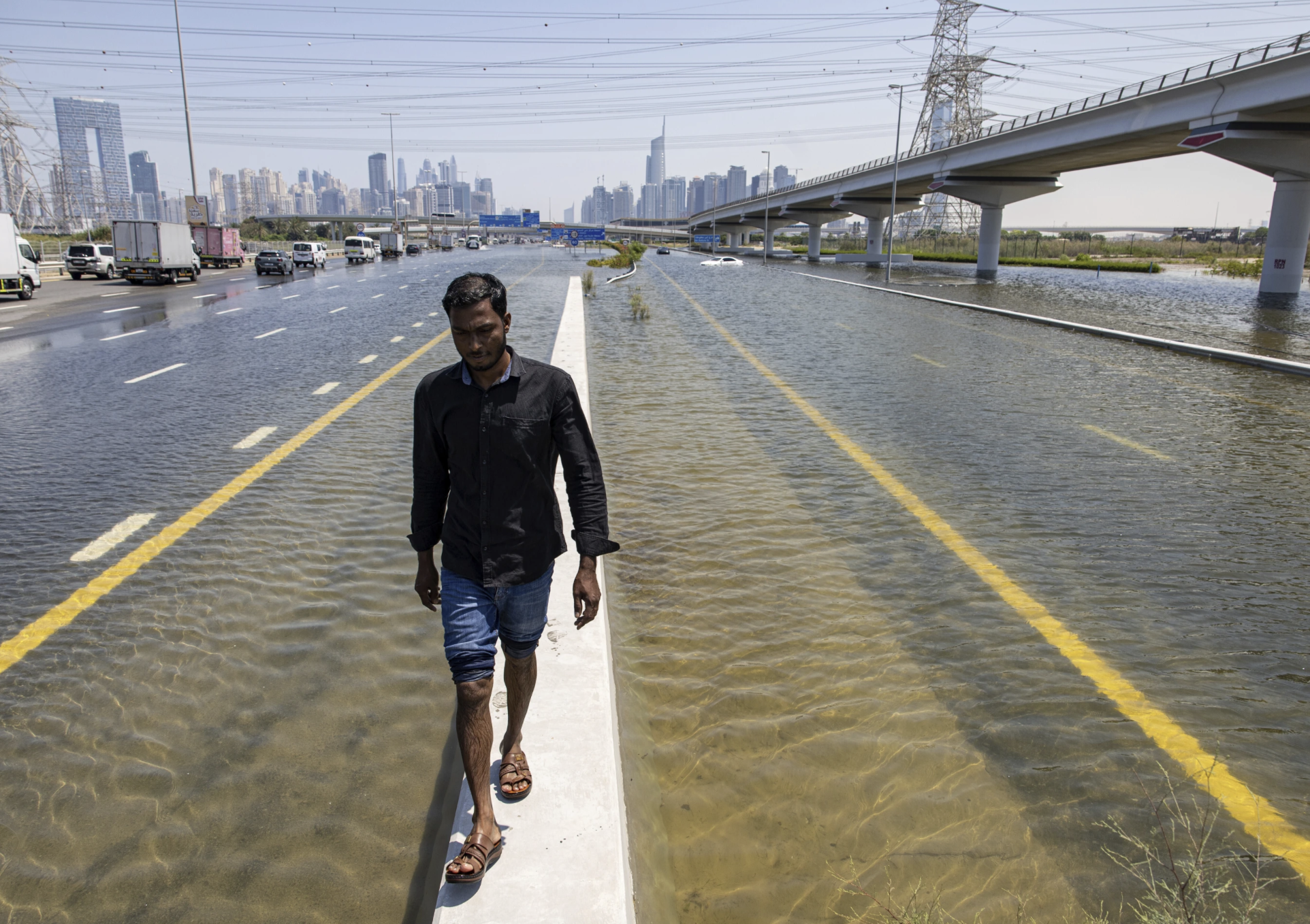 迪拜的高速公路上，一名男子在暴雨造成的洪水中沿着路障行走。（图源：社交媒体）